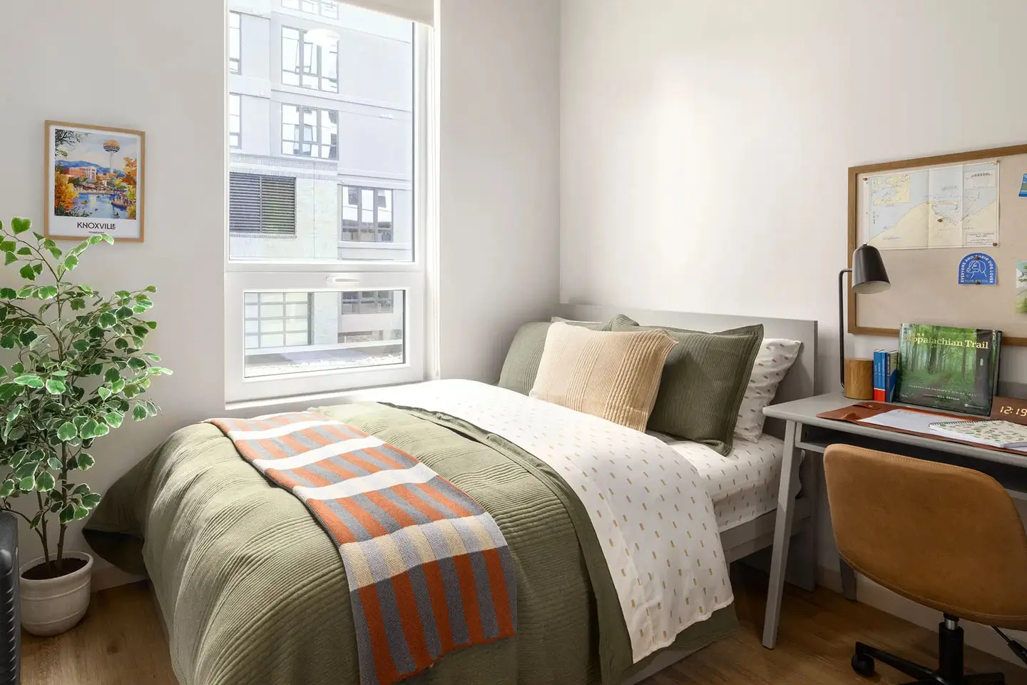 Decorated apartment bedroom with large mattress. desk, and bedside window.
